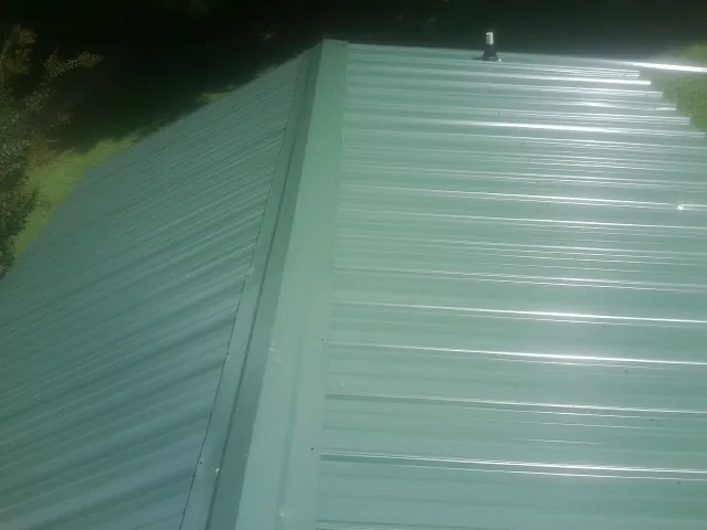 New green metal panels meeting at the ridge of a roof — Flat Roof Repair work by our crew in Lanoka Harbor