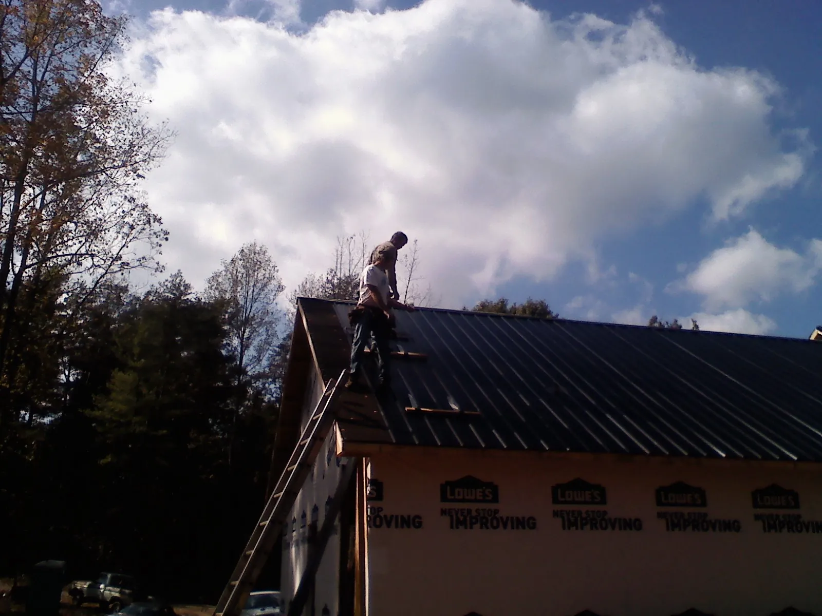 Roofer fastening dark metal panels high against a cloudy sky, from a Roof Inspection job in Lanoka Harbor