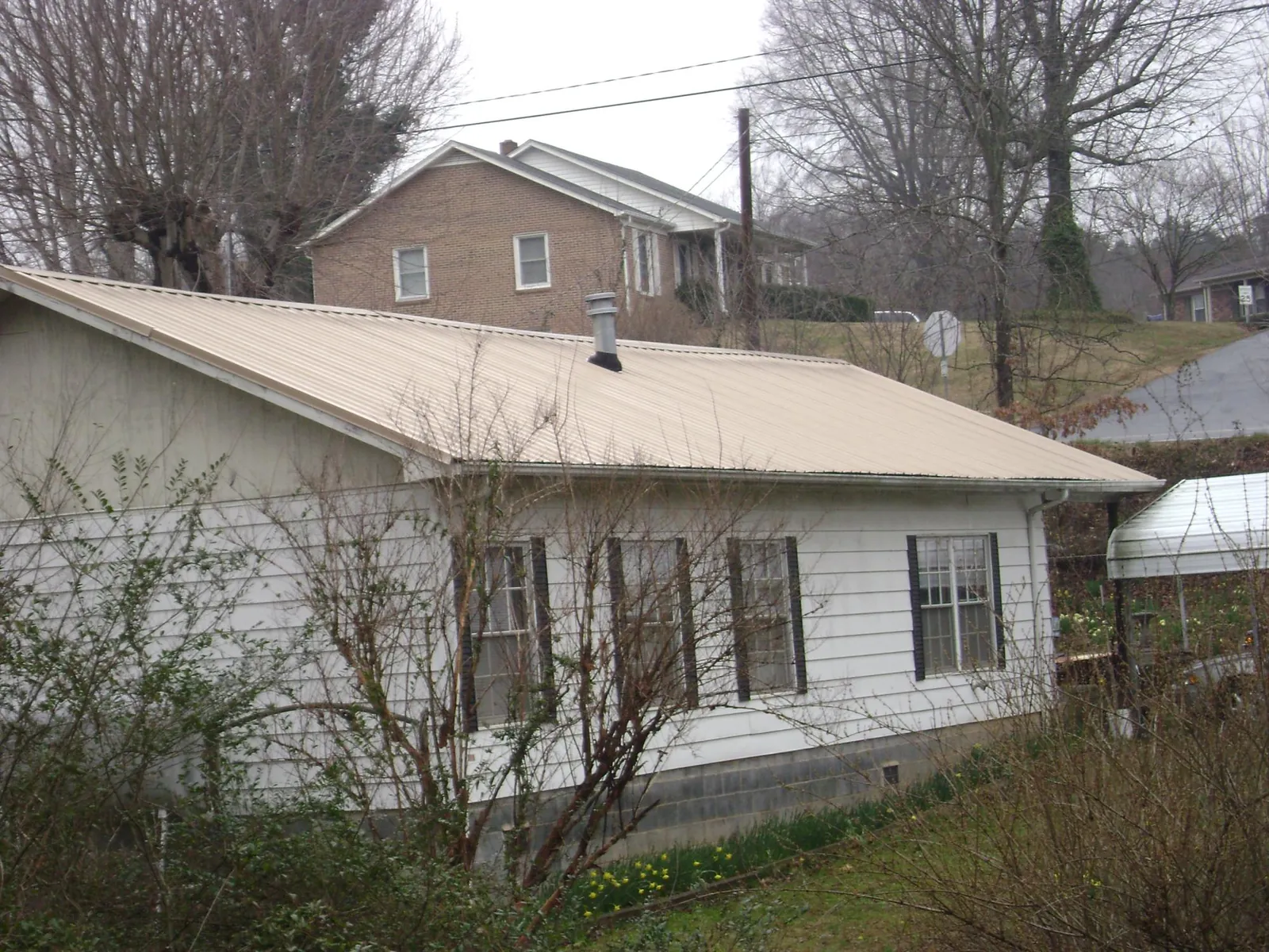 Tan metal roof on a white sided house set into a hillside — Commercial Roofing by Roofing Brothers in Lanoka Harbor